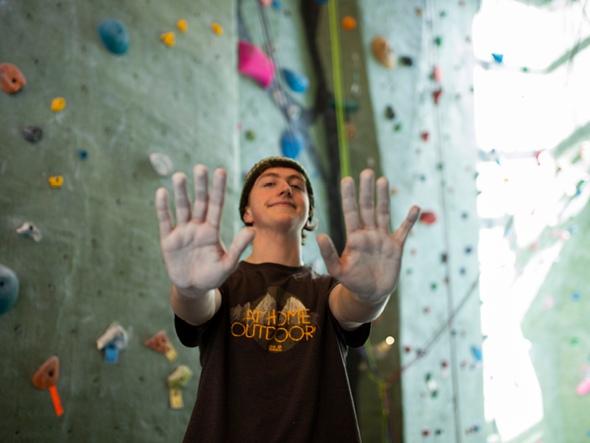 Student holding up hands that have chalk on them and the rock wall behind them