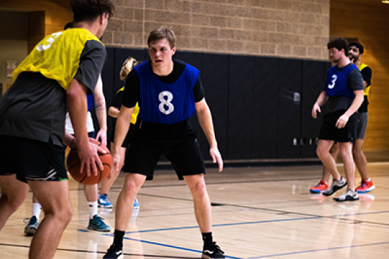 Intramural baskeball game, one students has the ball and another student is defending