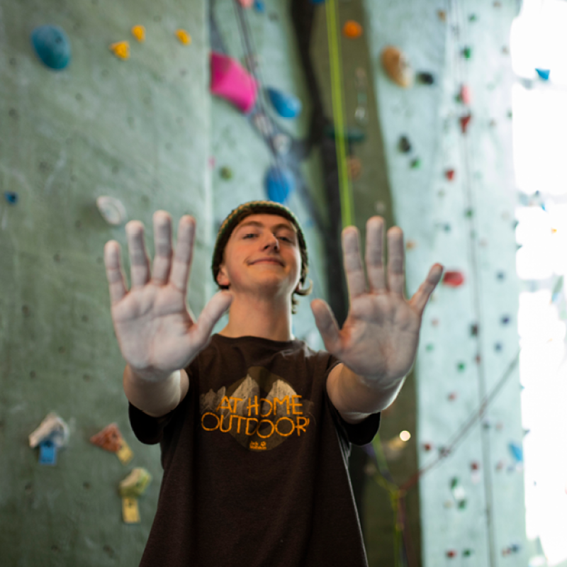student standing in front of climbing wall holding up his chalked hands