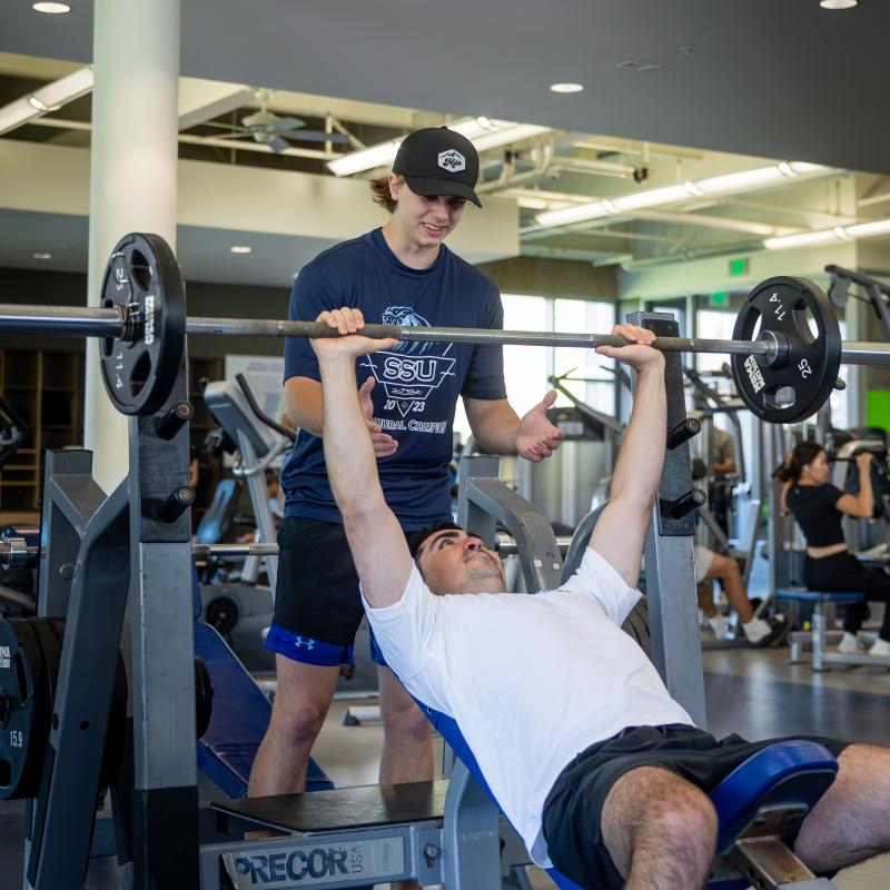 Student trainer helping another students lift the bench press bar