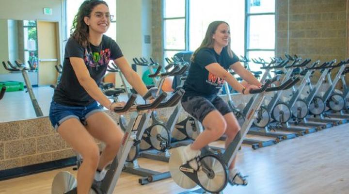 Two women riding stationary bikes in a gym.