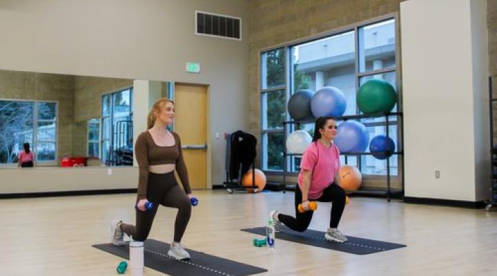 Two women performing lunges on yoga mats in a fitness studio.
