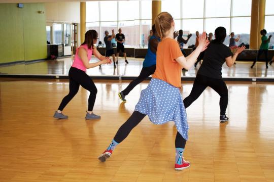 Group fitness class dancing in a studio with mirrored walls.