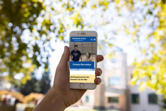 Person holding a smartphone displaying a university recreation website outdoors.